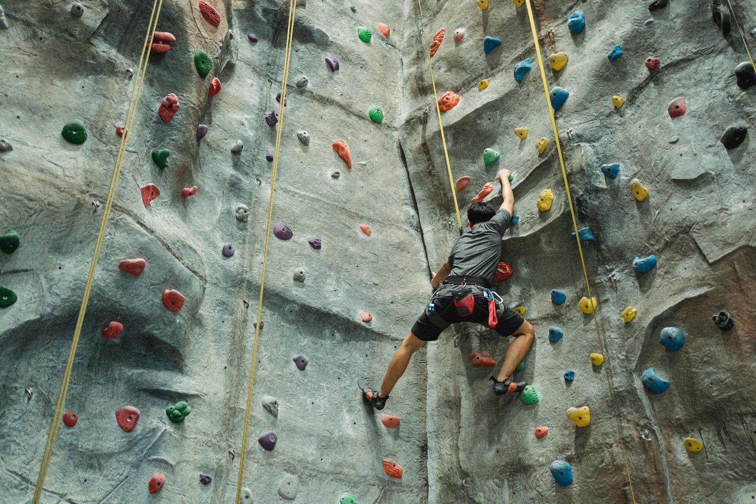 Adult male climber ascending a colorful indoor rock wall at a gym, showcasing strength and determination.